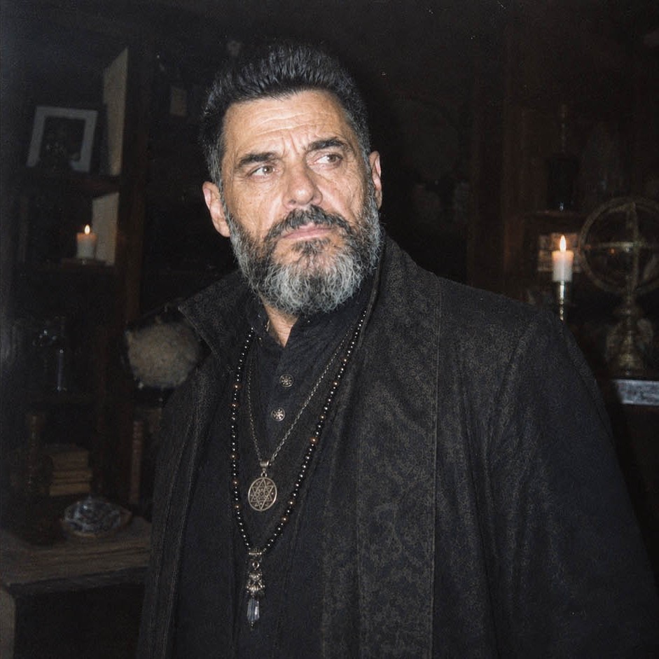 Victor Draconic Romanian witchcraft practitioner studying an old ritual manuscript in a candlelit occult chamber